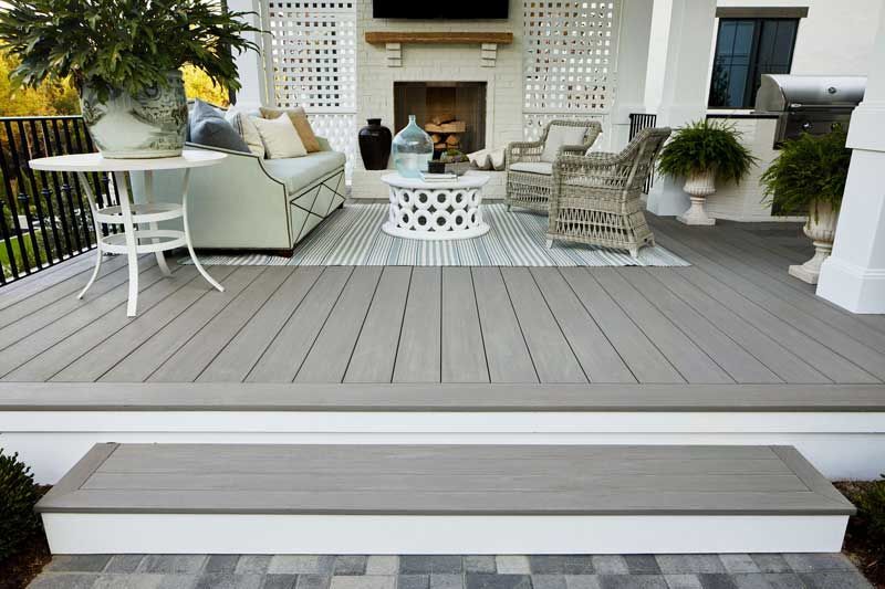 Grey composite deck with outdoor furniture on a porch, including a sofa, chairs, and fireplace.