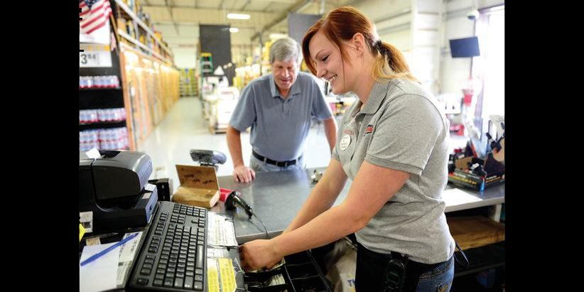 A woman is working on a computer while a man looks on.