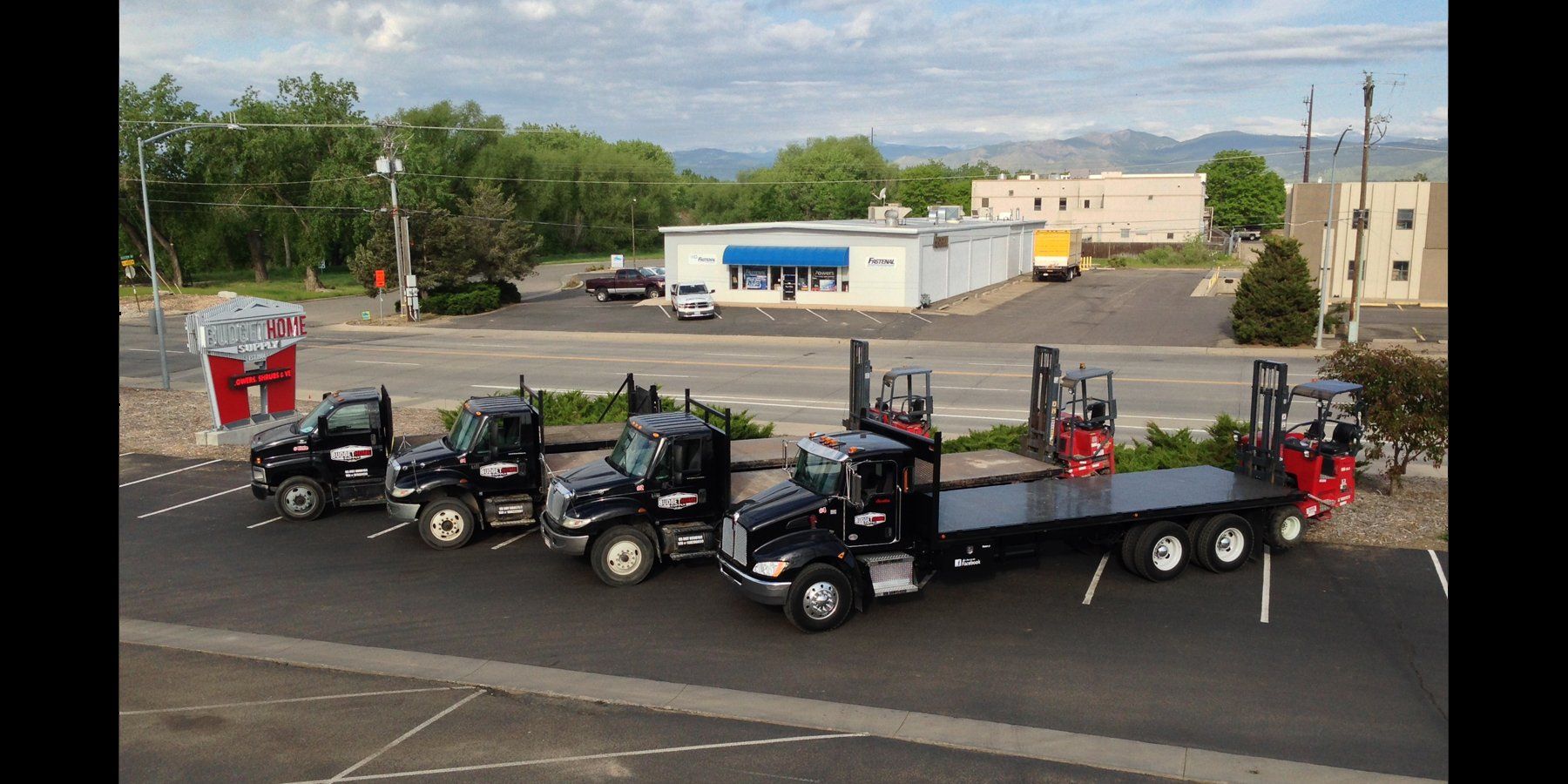 A row of flatbed trucks are parked in a parking lot.
