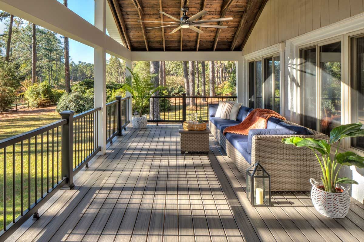 Trex® Decking from Budget Home Supply Colorado - Covered porch with seating, overlooking a yard and trees. Blue sofa, wicker furniture, and potted plant.