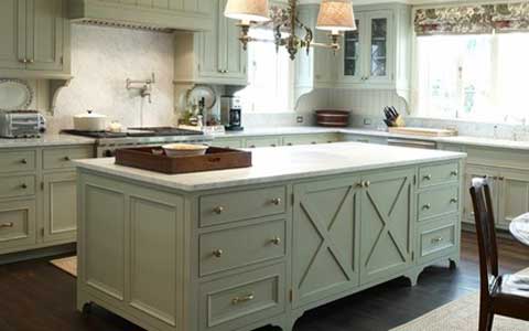 Green kitchen with island, marble countertops, brass hardware, and a chandelier.