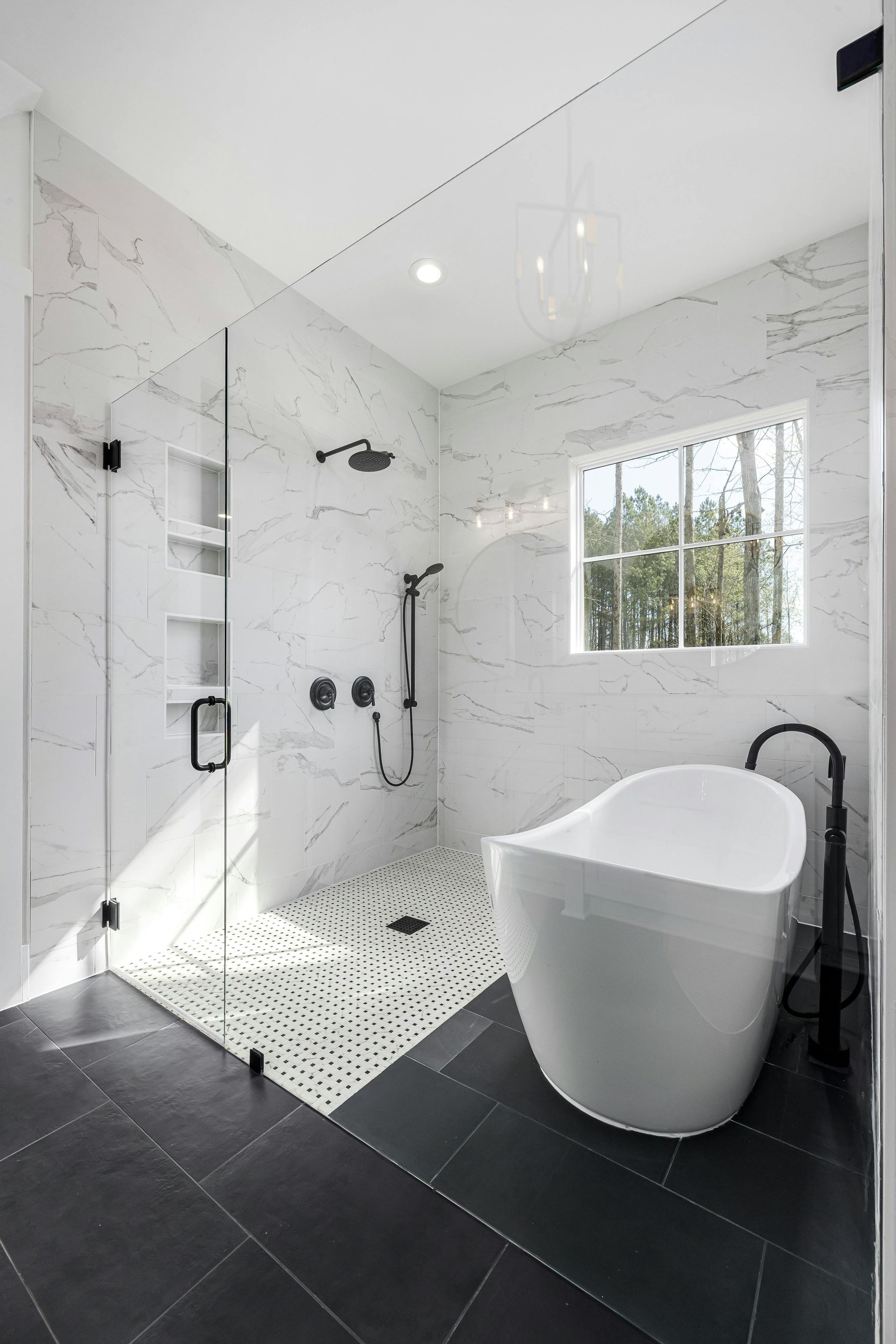Modern white bathroom with freestanding tub, walk-in shower, and black tile floor.