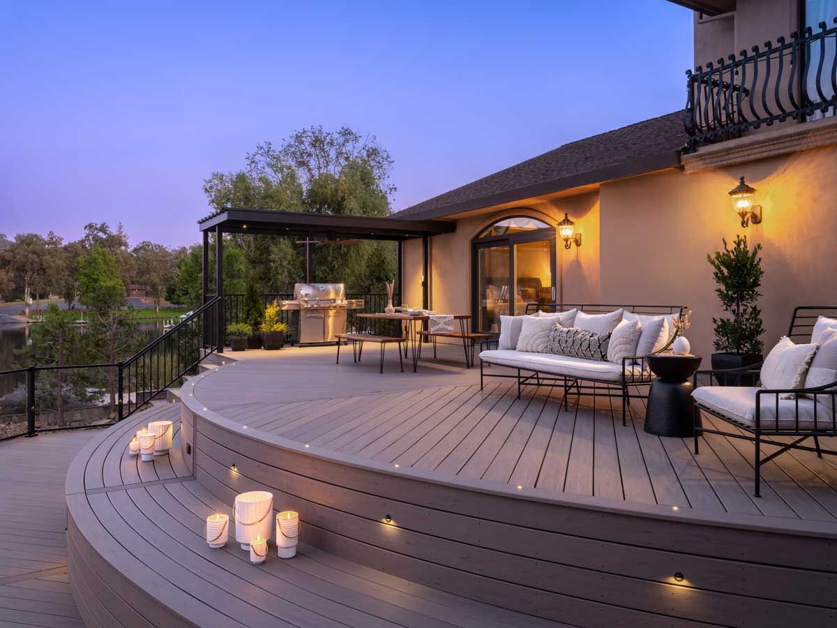 Trex® Decking from Budget Home Supply Colorado - Curved wooden deck with outdoor seating, grill, and candle-lit ambiance at dusk.