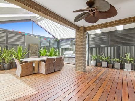 Covered outdoor patio with a dining table, grill, and ceiling fan. Wooden deck and brick columns.