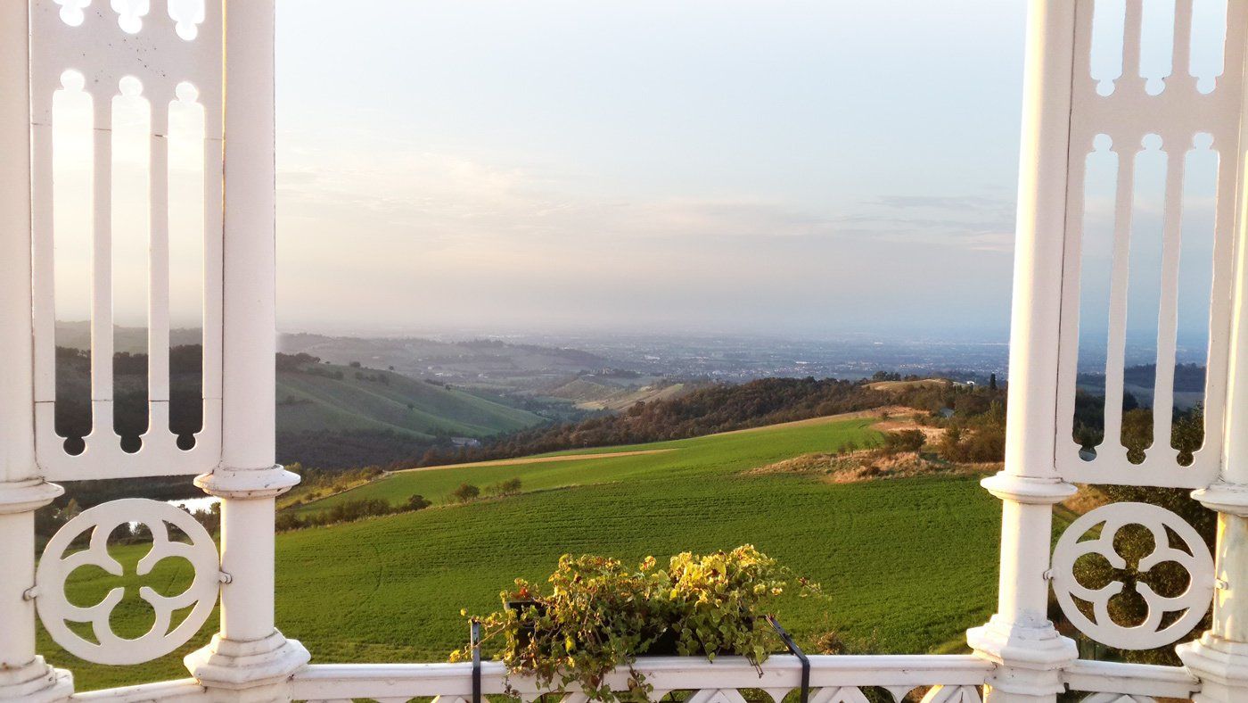 Framed view of rolling green hills and distant cityscape from a white ornate balcony at sunset.