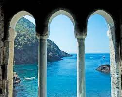 View of a turquoise cove through three stone archways overlooking the Italian coast.