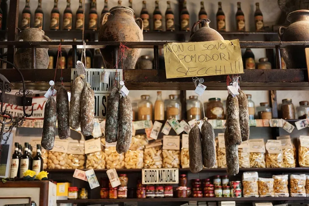 Italian deli with hanging salami and shelves of pasta and preserves.