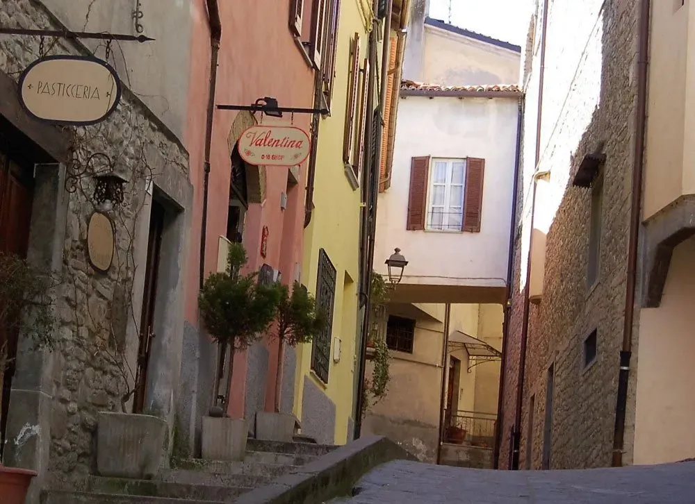 Narrow cobblestone alley in Italy with pastel buildings and small shop signs.