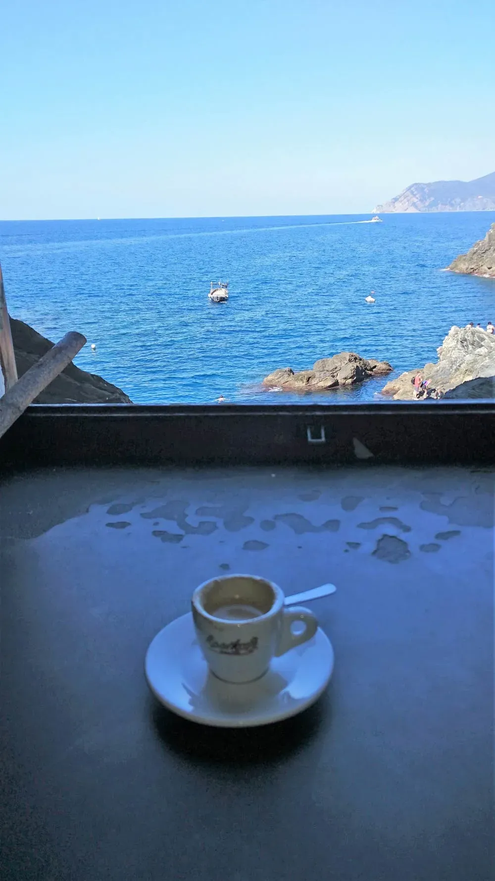 Espresso cup on a windowsill overlooking a rocky Ligurian coast and calm blue sea.