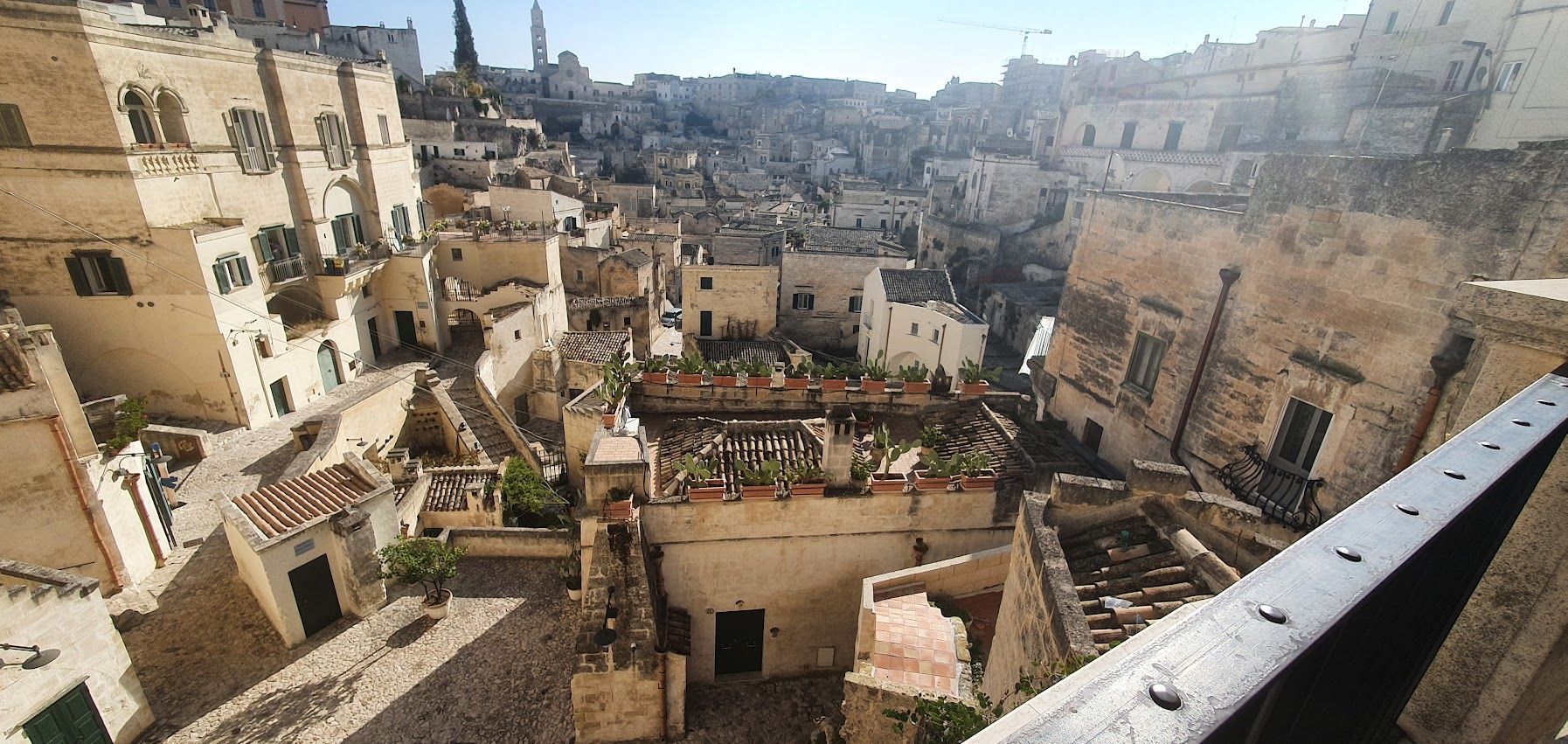A panoramic view of Sassi di Matera, showing ancient stone buildings, narrow alleys, and rooftop gardens with cacti.