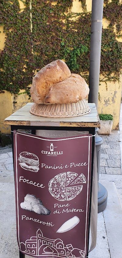 A large loaf of Pane di Matera displayed on a wicker tray above a sign advertising local baked goods.