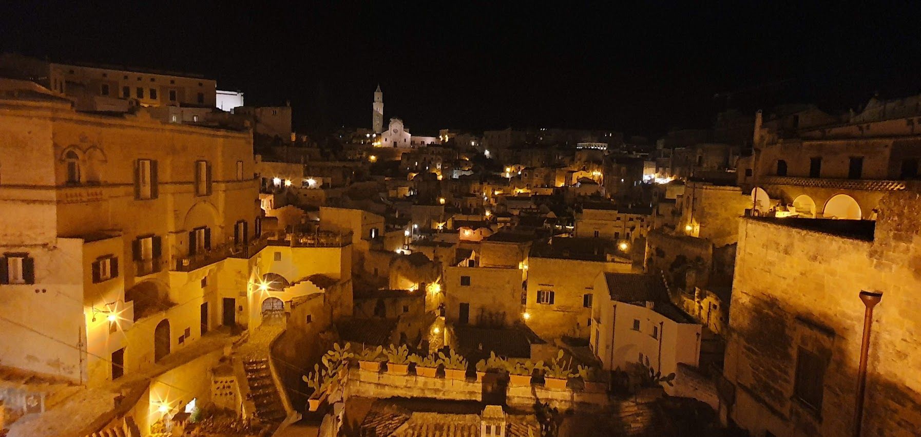 Sassi di Matera at night, with warm golden lights illuminating ancient stone buildings and narrow alleyways.