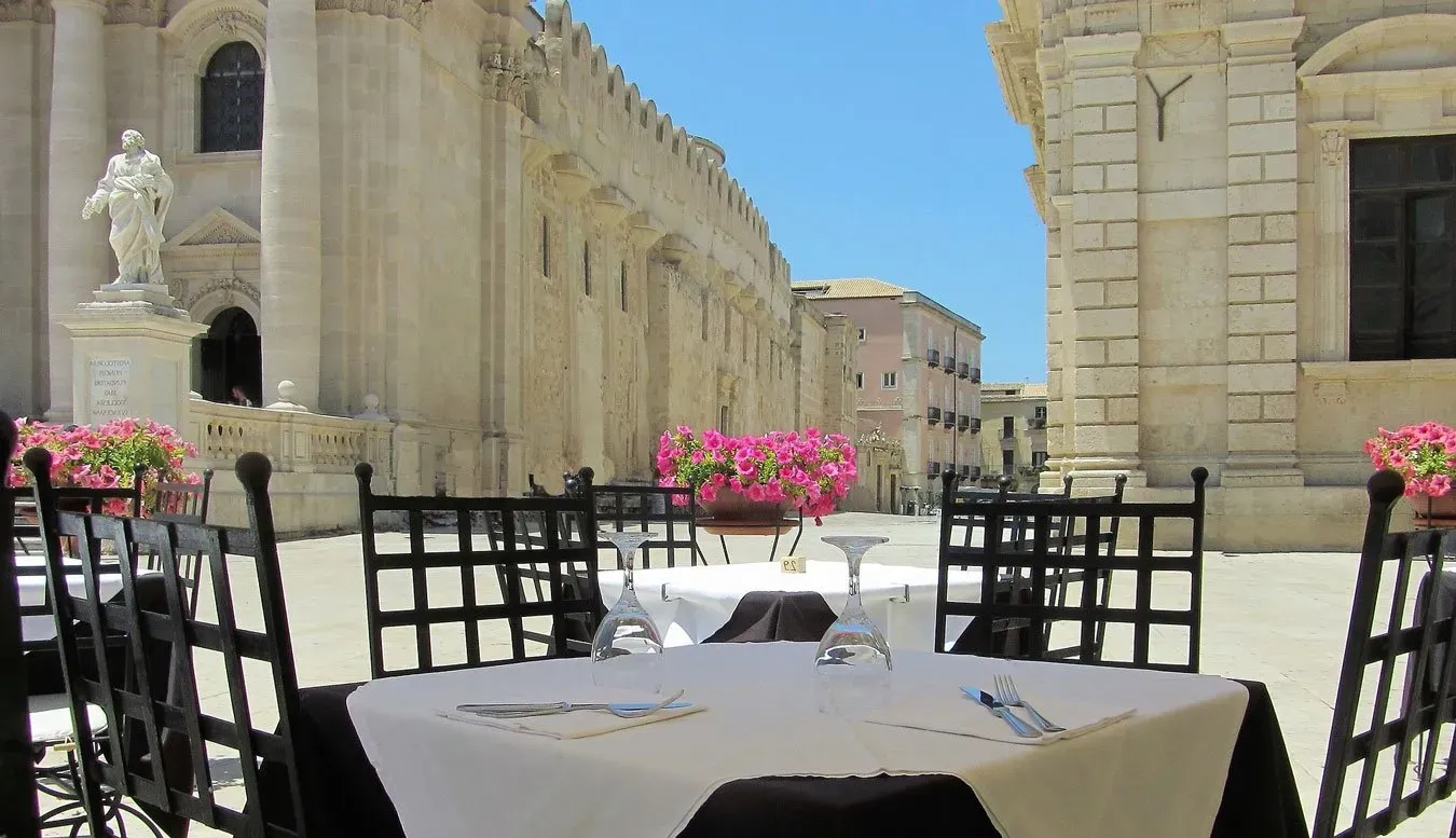 Sunny plaza café with flowers and historic buildings.