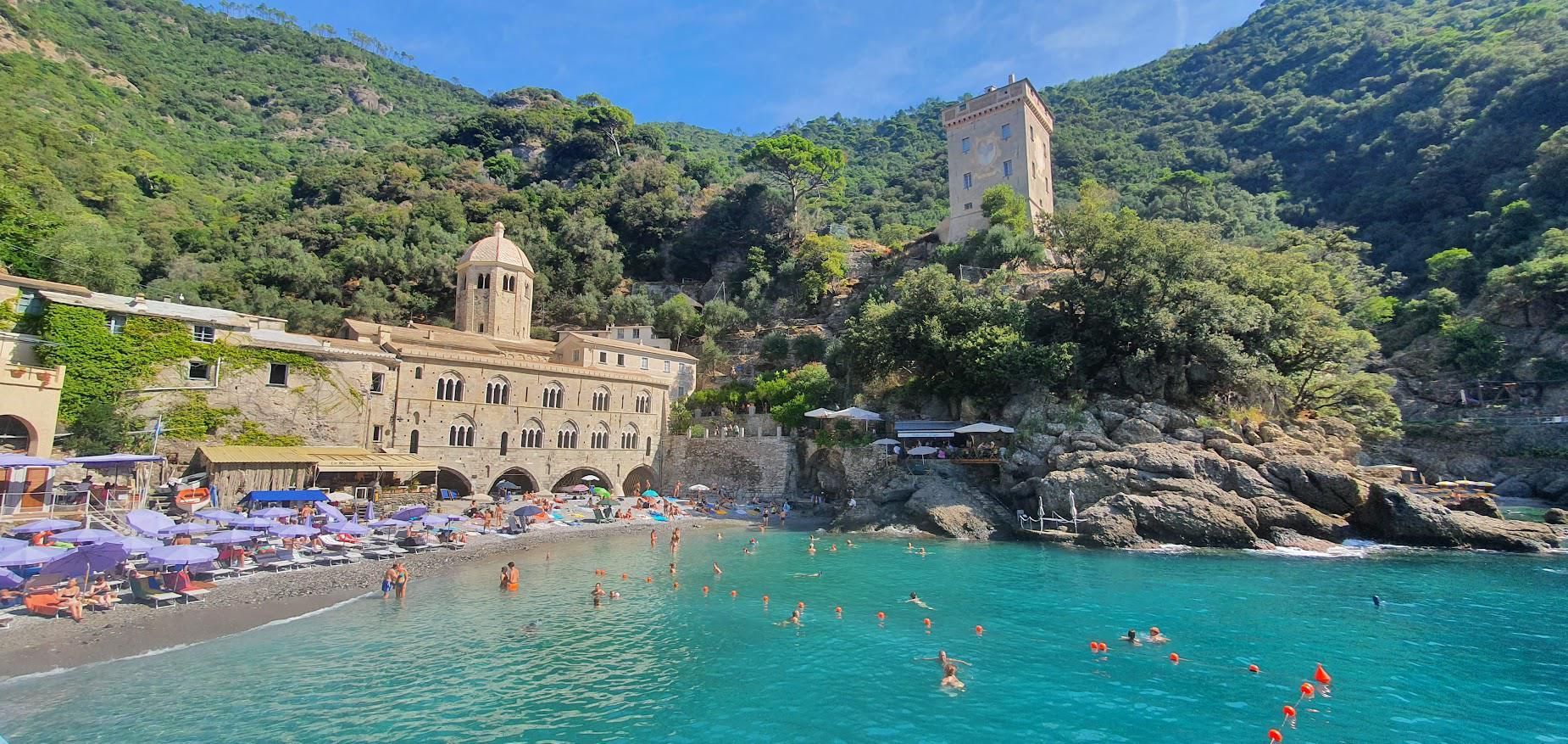 Swimmers enjoy clear blue water at San Fruttuoso beach, backed by an ancient abbey and lush hills.