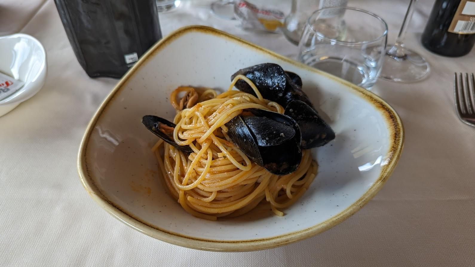 A bowl of spaghetti with mussels on a table.