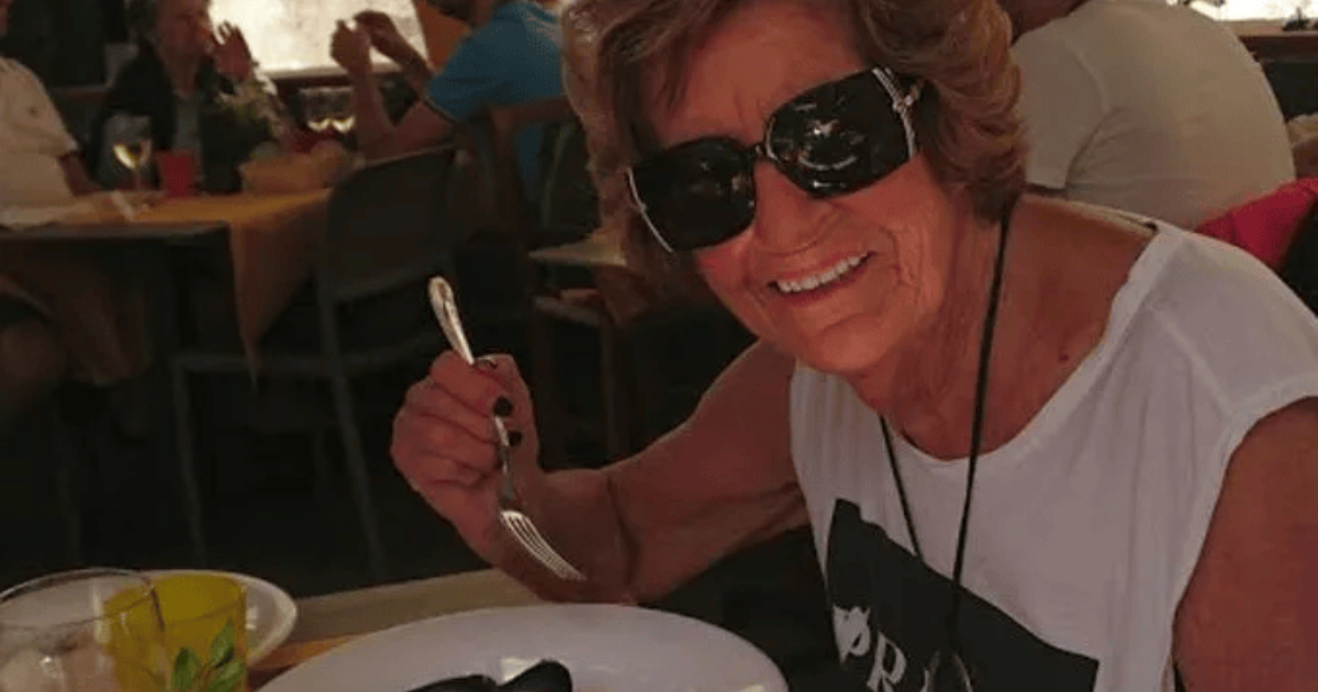 Woman in sunglasses smiling at a restaurant table while holding a fork and eating mussels.