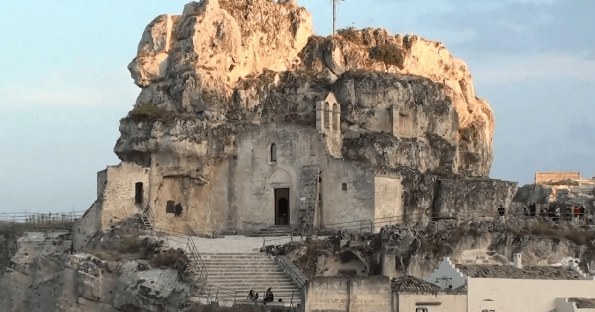 An ancient rock-hewn church in Sassi di Matera, carved into a limestone cliff, bathed in warm sunlight.