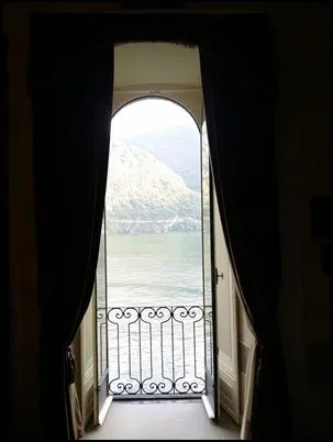 Open doorway with curtains framing a view of a lake and mountains through an ornate iron balcony.