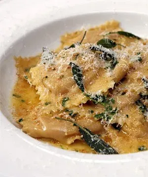 Plate of ravioli topped with grated cheese, herbs, and butter sauce.