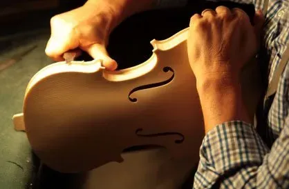 Artisan shaping a violin body by hand.