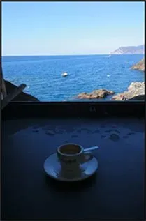 Espresso cup on a table overlooking the sea with rocky coastline and a boat in the distance.