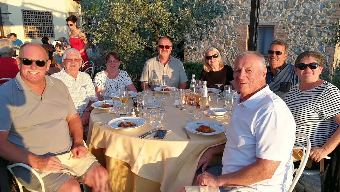 Group of tourists enjoying a pasta dinner outdoors in the late afternoon sun.