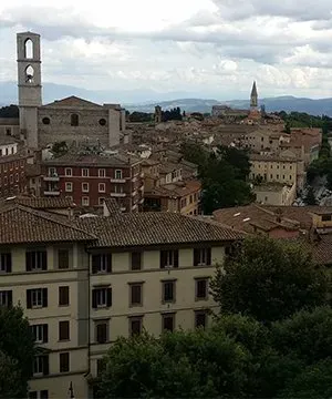 Hilltop view of Perugia with terracotta rooftops, historic stone buildings, and distant mountains under a cloudy sky.