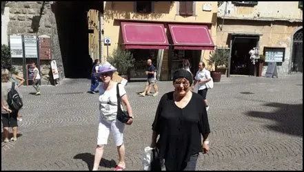 Two women walking across a cobblestone plaza in front of a building with pink awnings.