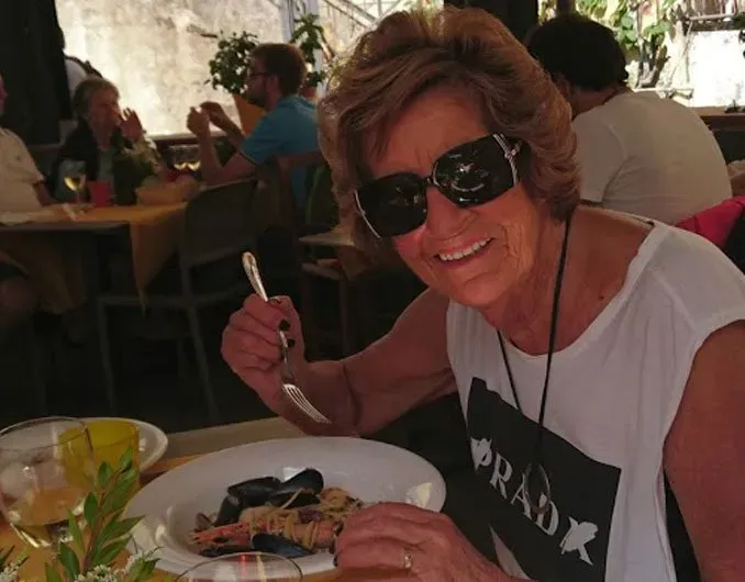 Woman in sunglasses smiling at a restaurant table while holding a fork and eating mussels.