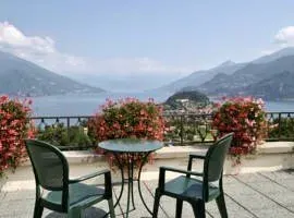 Patio with two chairs and a table overlooking Lake Como, surrounded by flowers and mountains.