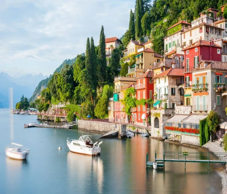 Colorful buildings of Varenna line the shore of Lake Como, with boats docked on the calm water.
