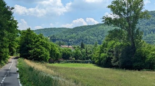 Winding road through lush green countryside with rolling hills and a distant village.
