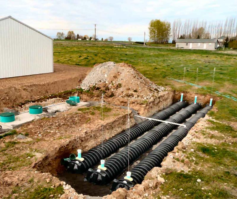A drainage system is being built in a field with a white building in the background