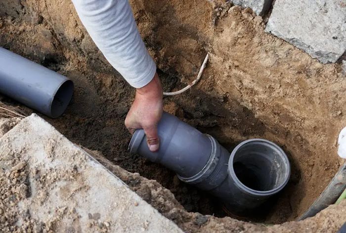 A person is holding a pipe in a hole in the ground.