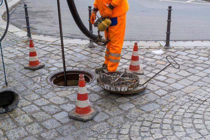 A man is working on a manhole cover on a cobblestone street.