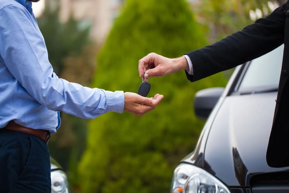 Una persona porge le chiavi dell'auto a un'altra accanto a un'auto nera all'aperto.