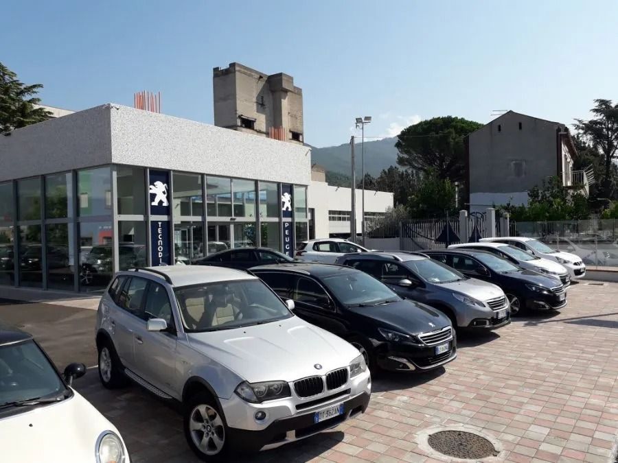 Parcheggio antistante un edificio con facciata in vetro, con una fila di auto parcheggiate sotto un cielo limpido.