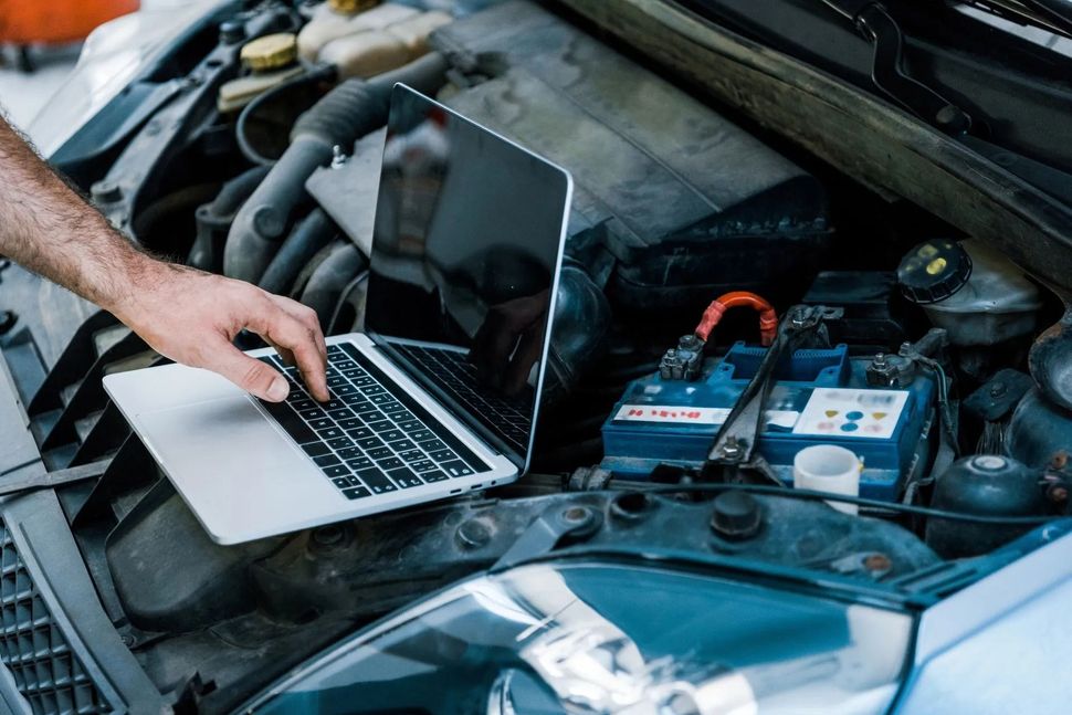 Persona che utilizza un computer portatile per diagnosticare un motore d'auto con il cofano aperto