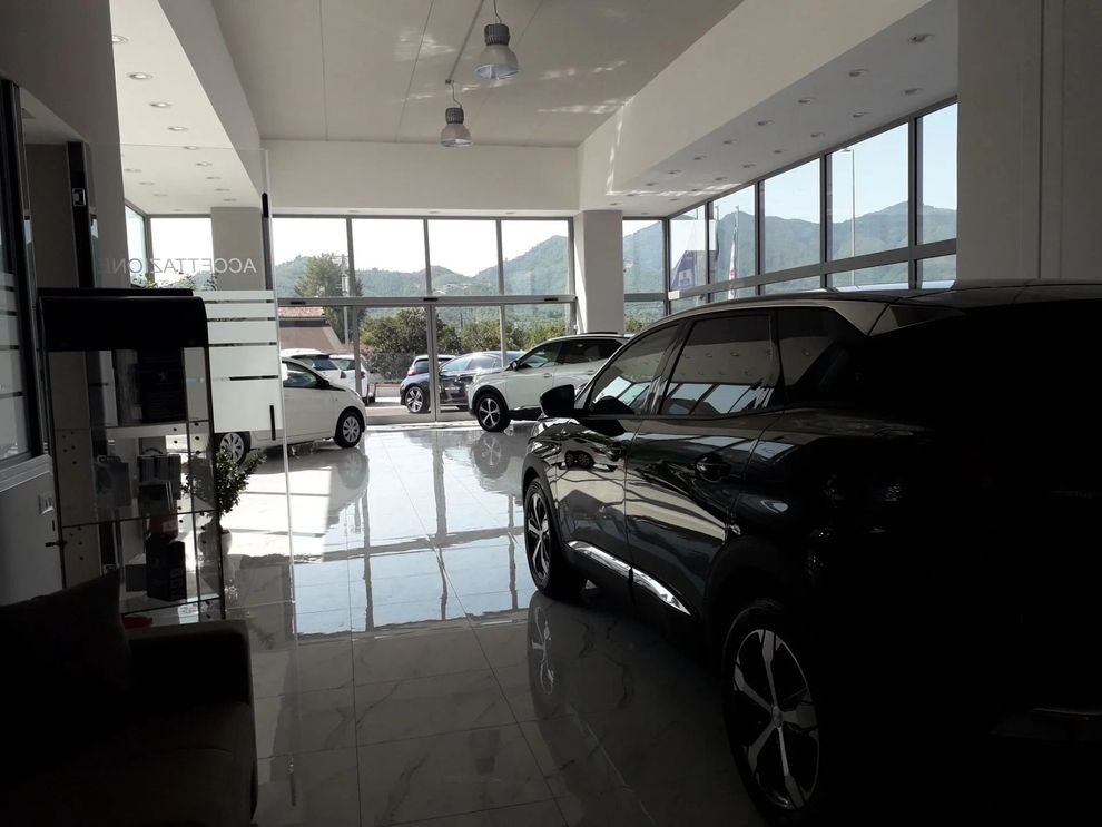 Showroom di automobili con pavimento in piastrelle lucide, SUV nero in primo piano e auto esposte vicino a grandi vetrine.