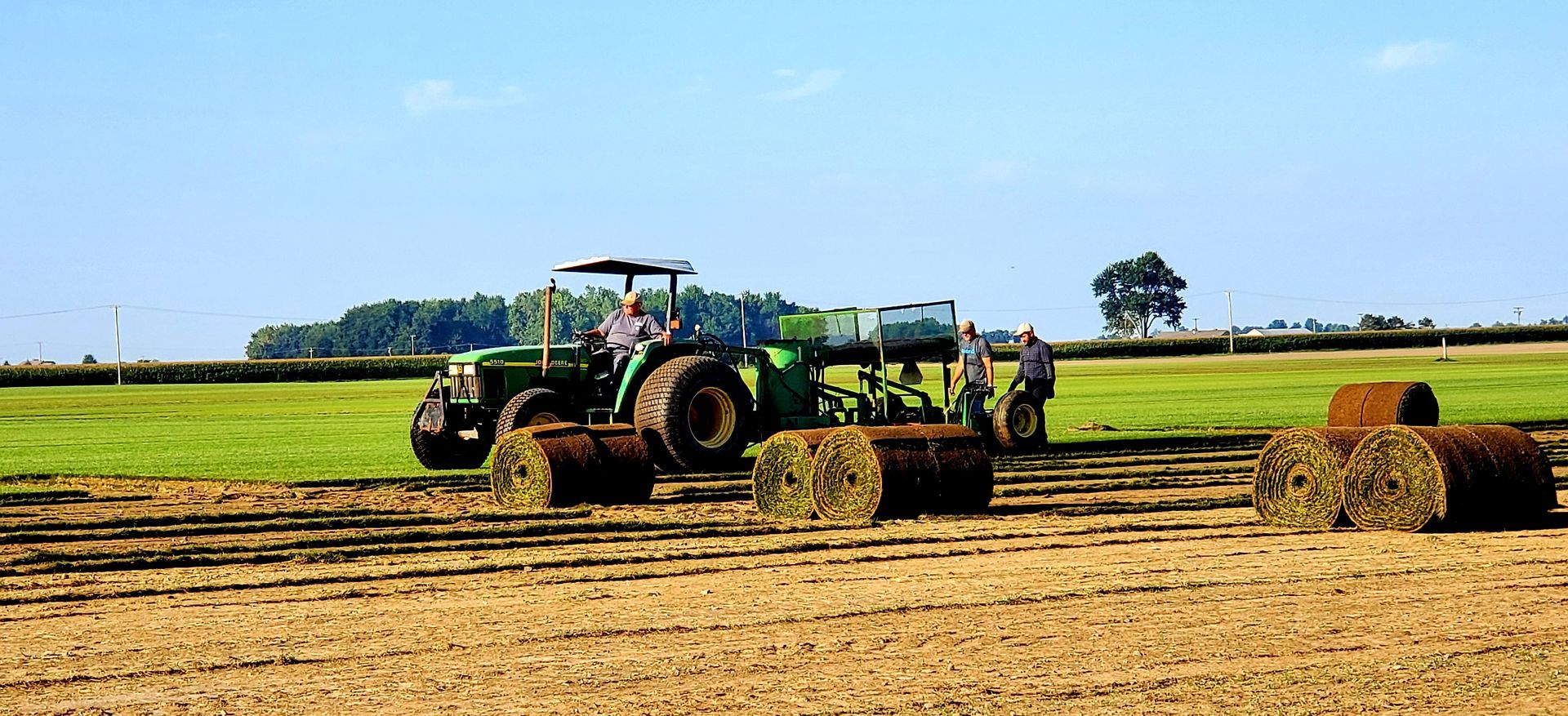 A tractor is rolling hay bales in a field.