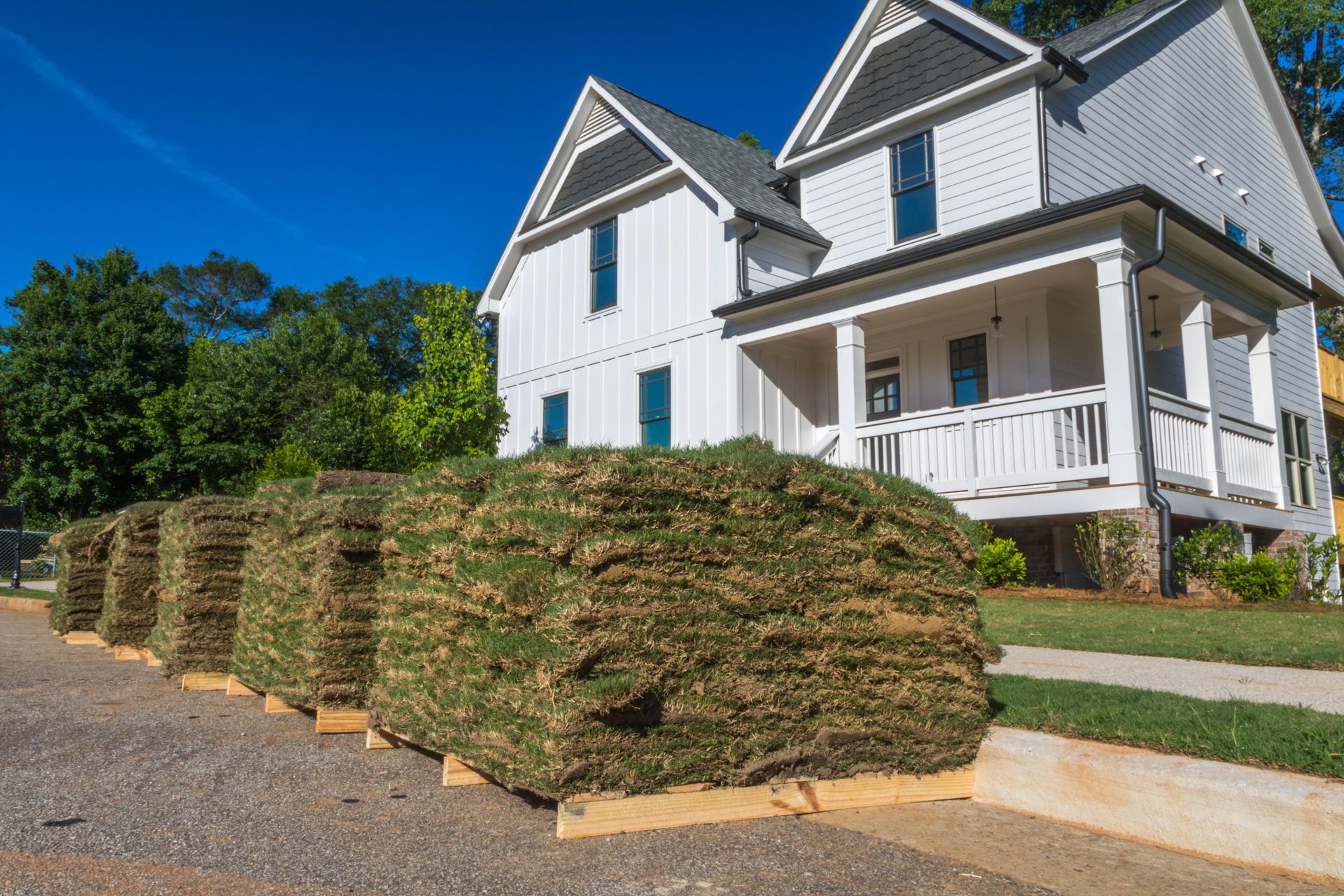 Stacked sod pallets outside a white house on a sunny street