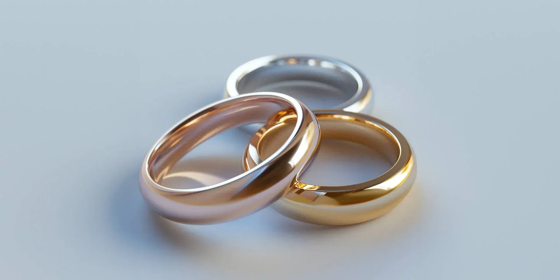 Three wedding rings: gold, rose gold, and silver, resting on a light gray surface.