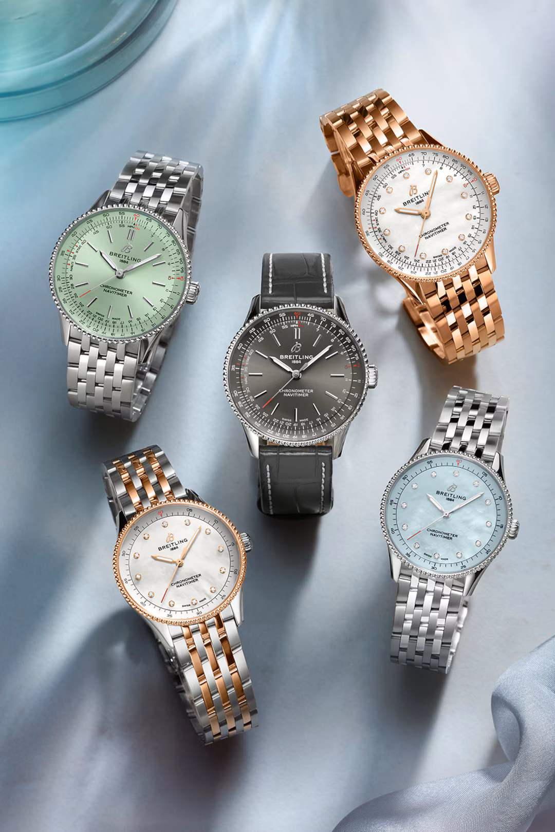 Five elegant wristwatches on a reflective surface. Various colors: silver, rose gold, and black with intricate watch faces.