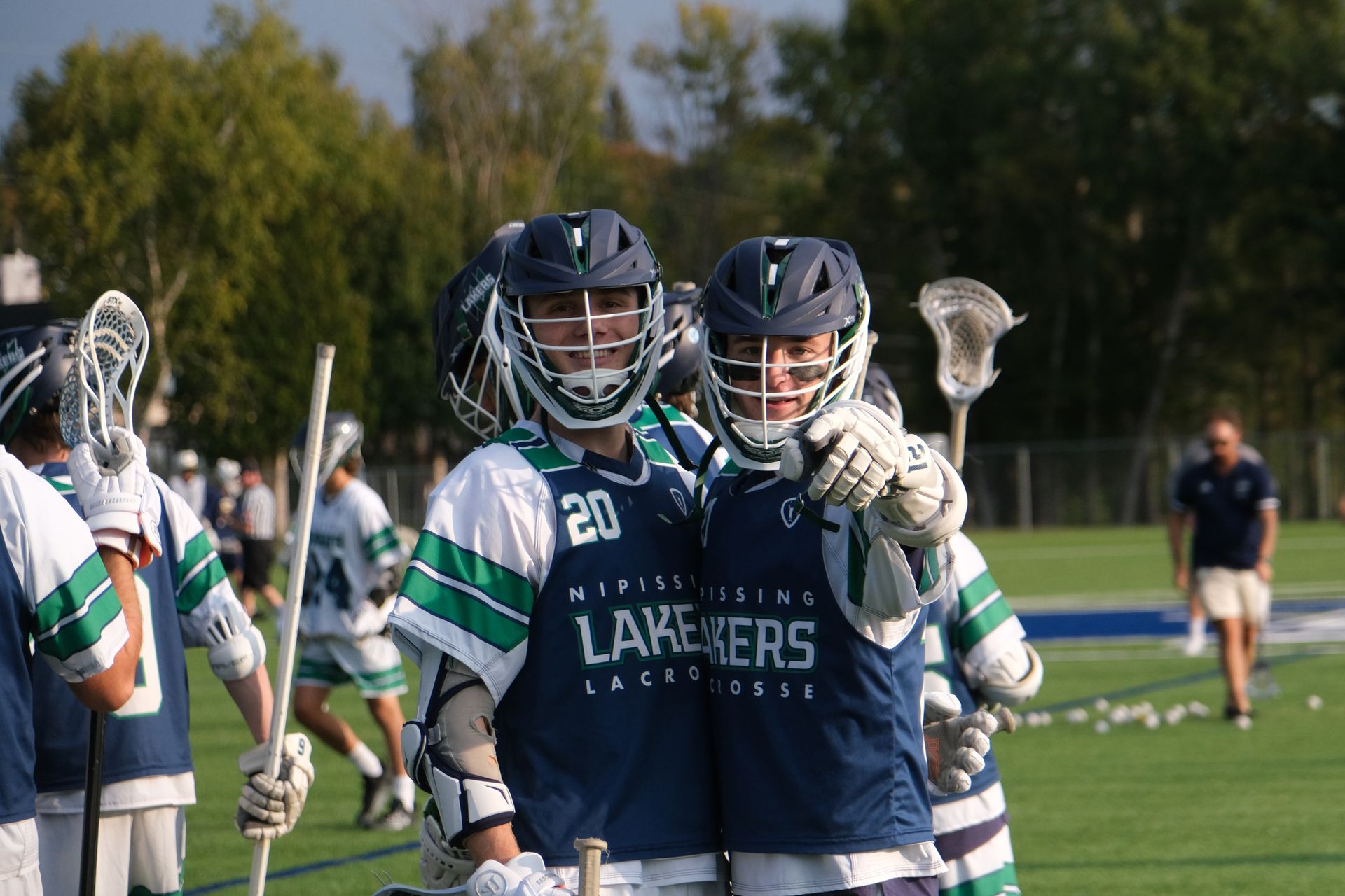 Two lacrosse players in navy and green jerseys, Lakers team, smiling, outdoors.