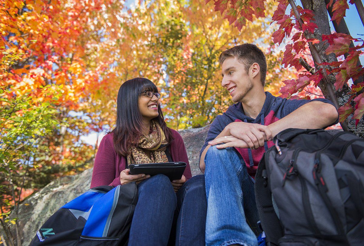 A man and a woman are sitting on a rock looking at a tablet.