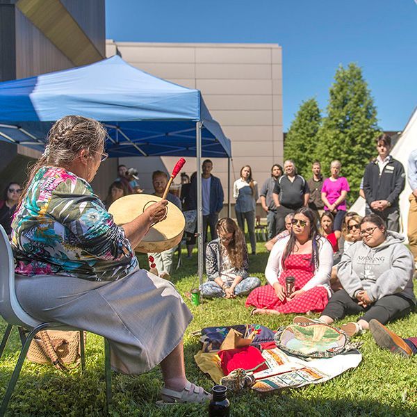 A woman is sitting in a chair playing a drum in front of a group of people.