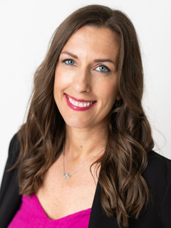 Smiling woman with long brown hair in a pink top and black blazer against a white background