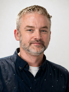 Portrait of a man in a navy shirt, facing the camera with a slight smile on a light background
