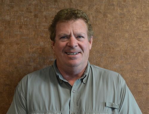 A man wearing glasses and a yellow shirt is smiling for the camera
