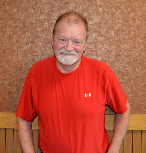 A man wearing glasses and a yellow shirt is smiling for the camera